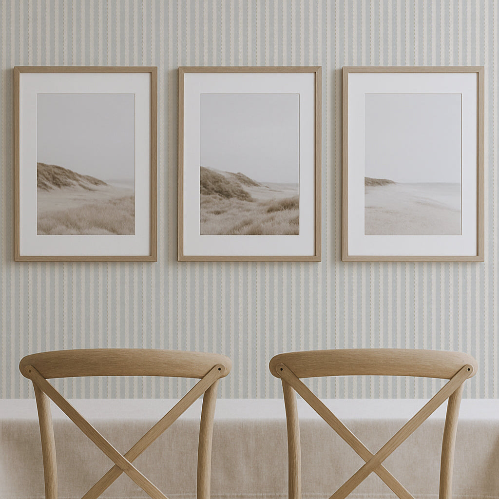 Two wooden chairs with beige cushions in front of a wall with three framed beachscape prints.